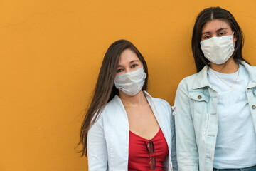 Multiracial female friends wearing protective masks looking at the camera as they walk together down the city street on a sunny day.