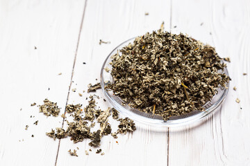 Fermented tea made from raspberry leaves in a glass plate on a white wooden table. Composition with organic, natural, dry herbal tea