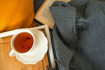 Close-up of cup of tea on the tray , with book and blanket. Home cozy decor