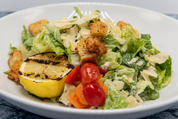 Caesar salad served with a grilled lemon half covered in dressing and presented in a bowl.