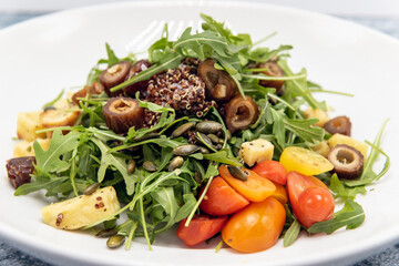 Arugula salad generously piled onto a plate topped with tomatoes and quinoa.