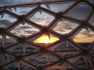 Landscape of a northern fiery scarlet sunset on a sailing yacht in the Arctic, Antarctica through icy ropes, rails, fences