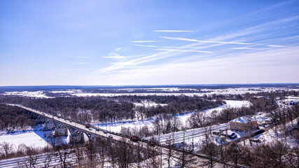 Landscape with transport arteries in winter. Road bridge, railroad, river, airplane tracks in the sky