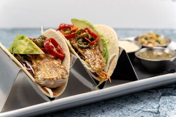 Pair of grilled fish tacos loaded with fillings and topped with fresh avocado wedges.