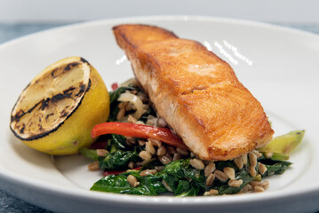 Pan roasted salmon seasoned perfectly on top a pile of barley and garnished with grilled lemon slice.