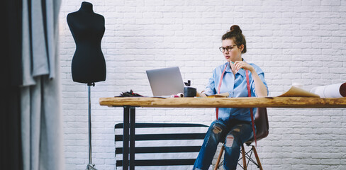 Young dressmaker browsing laptop in fashion studio