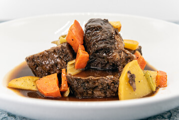 Beef short ribs drenched in a sauce and covered in carrots on other root vegetables.