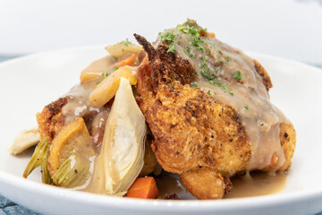 Braised chicken piled onto a plate covered in gravey sitting on top a bed of vegetables.