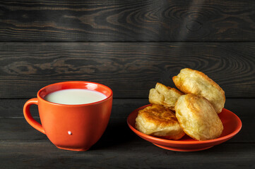 Milk mug and orange plate with homemade donuts on dark vintage boards. Idea for delicious festive breakfast or dinner