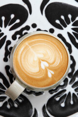 A cup of hot coffee cappuccino with heart shape on the table.