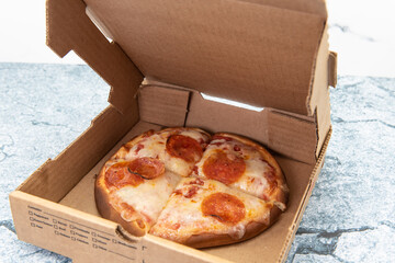 Small personal pan pizza cut into four slices and delivered in cardboard box.