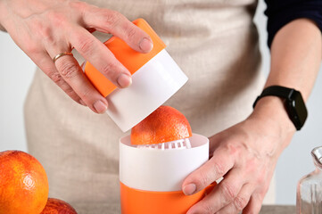 The woman put half an orange in a juicer and prepares to squeeze the juice out of it.