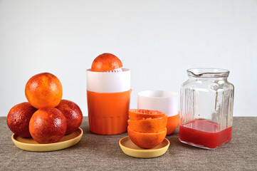 Manual juicer. There are several oranges nearby. There is a decanter with squeezed juice.