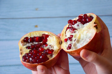 Kid hands hold broken pomegranate fruit on wooden blurred background