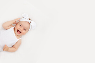 portrait of a smiling baby girl on a white bed at home, the concept of a happy, healthy baby, a place for text - obrazy, fototapety, plakaty