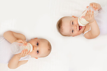 twin babies boy and girl with a bottle of milk on a white bed at home, baby food concept, place for...