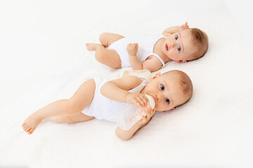 twin babies boy and girl with a bottle of milk on a white bed at home, baby food concept, place for...