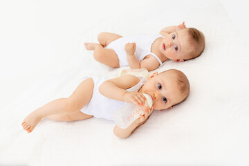 twin babies boy and girl with a bottle of milk on a white bed at home, baby food concept, place for text