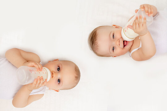 twin babies boy and girl with a bottle of milk on a white bed at home, baby food concept, place for text