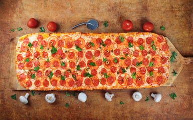 .Long pizza with salami and tomatoes lies on a wooden table. Roman pizza on a wooden shovel. One...
