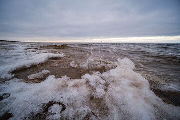 icy winter beach near the sea with frozen sand and ice blocks in the water