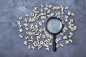 Magnifying glass with wooden alphabet on gray concrete background. Education concept. Flat lay....