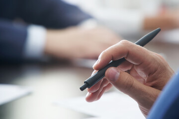 Professional male: politician, lawyer, teacher or office worker holds a ballpoint pen during a meeting, talking with partners, or discussing business strategy. Close-up