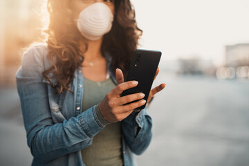 Young woman with protective face mask standing on empty city street  and using phone. Healthcare, Coronavirus protection, allergy protection concept.