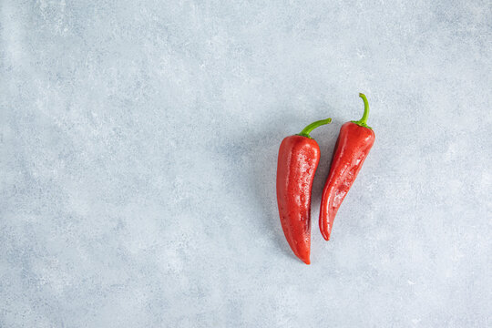 Fresh raw sweet red pepper kapi with water drops on light gray stone background, two peppers on gray table surface.