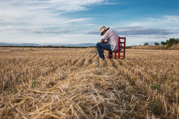 Naklejka na ściany i meble Farmer sitting on a chair looking at the field and sunset, local farming concept.