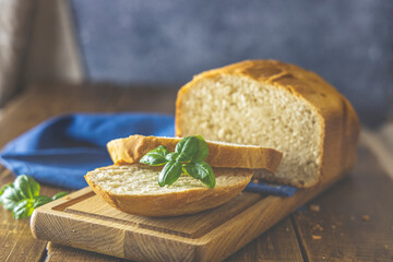 Loaf of freshly baked bread with basil and bread slices on wooden board over rustic wooden table background. Shallow depth of field.
