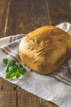 Loaf of freshly baked bread with basil on linen towel over rustic wooden table background. Shallow depth of field.