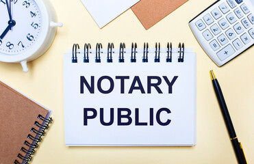 On a light background, a white alarm clock, a calculator, a pen and a notebook with the text NOTARY PUBLIC. Flat lay