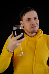 Relaxed young man poses with glass of red wine on black background. Adult happy guy resting with alcohol in his weekend.