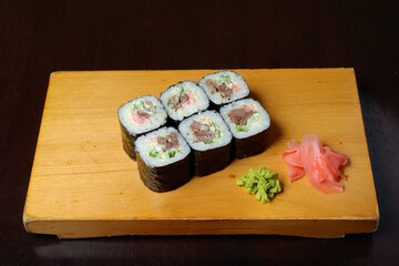 avocado tuna rolls wrapped in nori ginger wasabi leaves served on a wooden stand on a dark background