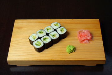 rolls with cucumber wrapped in nori ginger wasabi leaves served on a wooden stand on a dark background