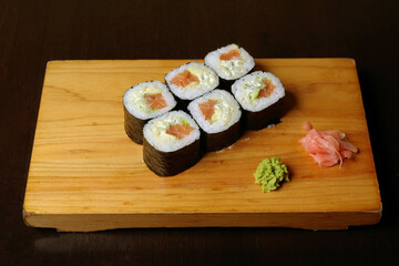 rolls of salmon cream avocado cheese wrapped in nori leaves useful food on a wooden stand on a dark background