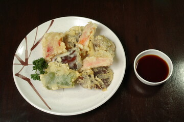 the vegetables fried in batter in a plate with sauce it is isolated a dark background