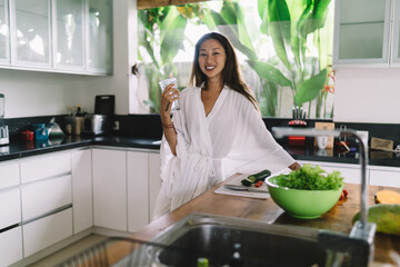 Smiling Asian lady standing in modern kitchen