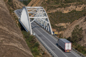View of a path that passes between some cuts in the mountain and an iron bridge through which a truck with a refrigerated semi-trailer circulates.
