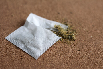 Chamomile teabag on cork board. Torn teabag with chamomile tea leaves spilling out