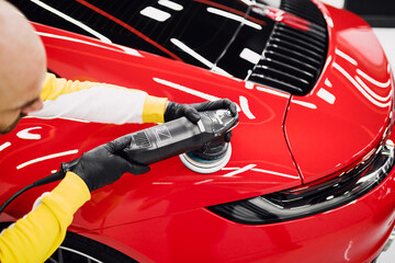 Car detailing - Worker with orbital polisher in auto repair shop. Selective focus.