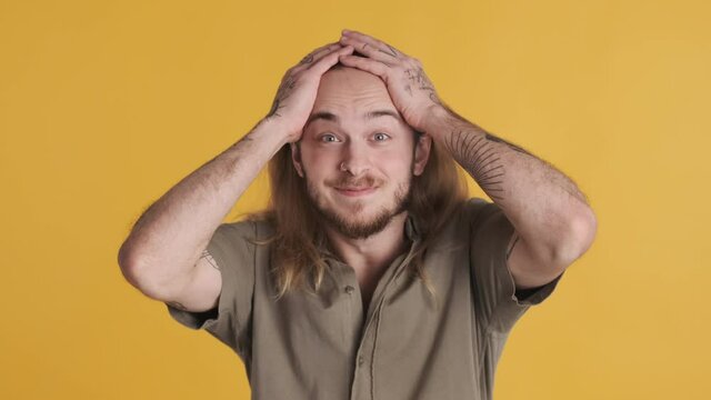 Surprised blond berded guy keeping hands on head smiling of hearing unreal news isolated on colorful background