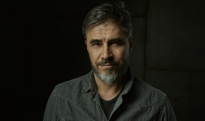 Portrait of casual older man with beard against dark background.