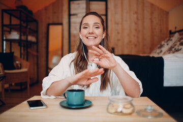 Screen application view of smiling young woman sit at table with laptop and talking on video call with friend or co worker, happy female with cup of tea or coffee speaking online on webcam conference