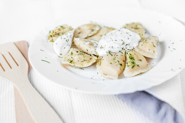 dumplings with potatoes and sour cream in a white plate.