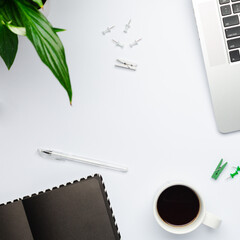 Workplace at quarantine time, empty dark notebook with a cup of coffee on white table. White color working space with laptop, minimalism.