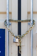 A heavy duty industrial size padlock was attached to steel chains at the entrance of an outdoor container that stores tools and equipment. Versatile image for locking, safety, security related concept