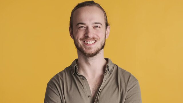 Young attractive bearded man looking happy sincerely smiling on camera over yellow background. Happy face expression