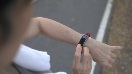 asian senior elderly woman touching smart watch activity tracker at park under tree. finger tapping sport watch for calories and heart rate information. slow motion orbit shot. health care top view. - Powered by Adobe